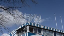 A modern building with blue and white geometric patterns and a Soho sign on the roof against a clear sky.