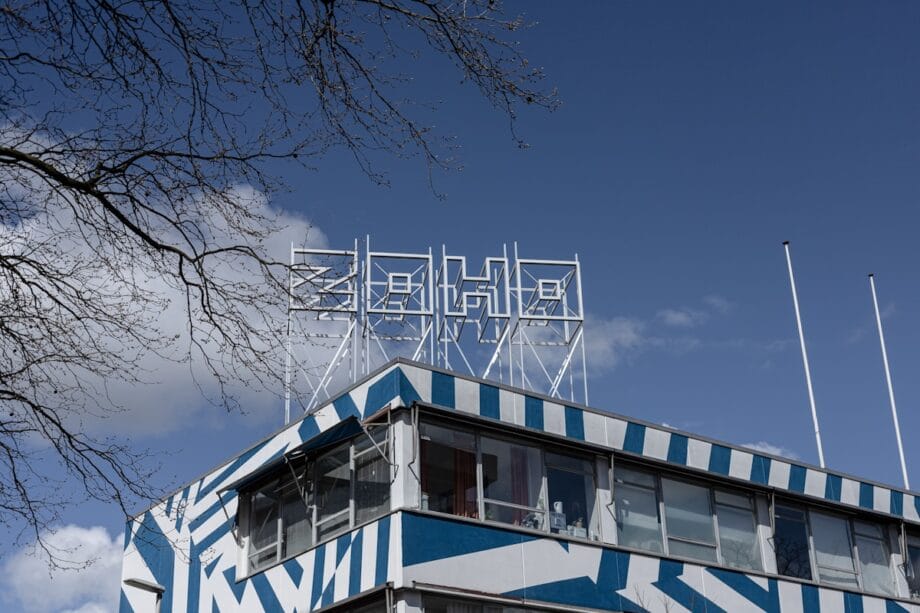 A modern building with blue and white geometric patterns and a Soho sign on the roof against a clear sky.