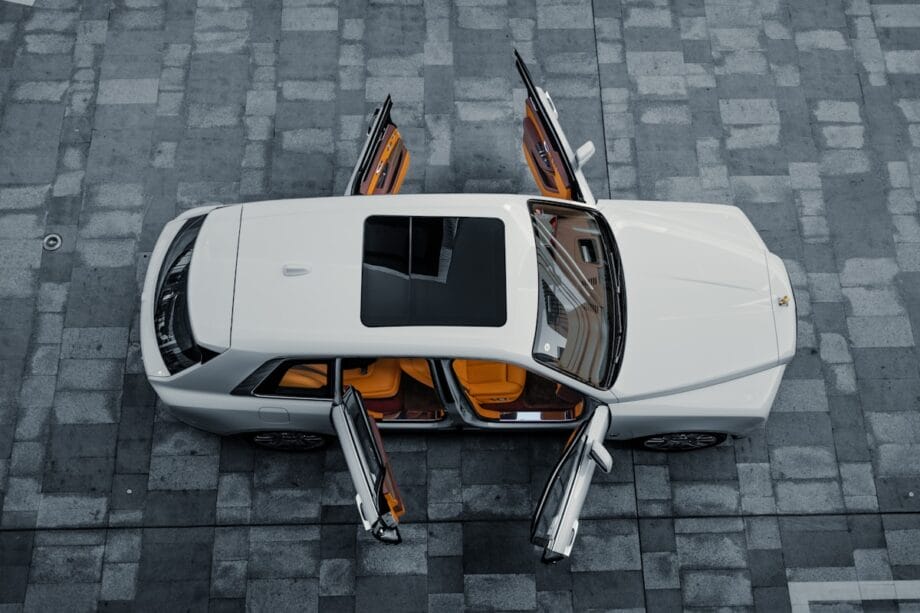 A white car with all four doors and the sunroof open, viewed from above, parked on a stone-tiled surface.