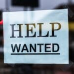 A paper sign reading HELP WANTED is taped to a glass window, indicating a job opening.