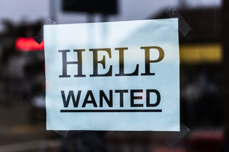 A paper sign reading HELP WANTED is taped to a glass window, indicating a job opening.