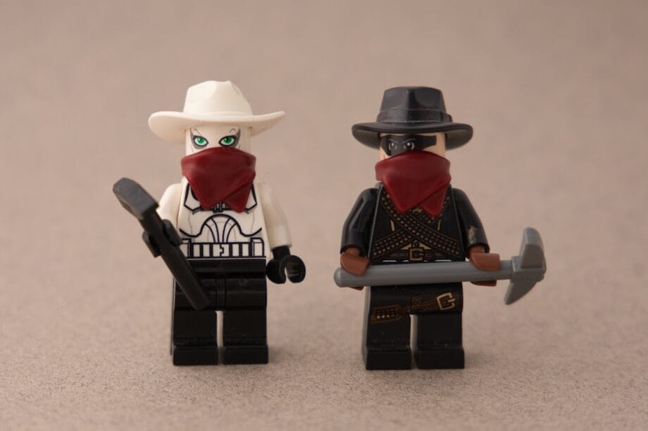 Two LEGO minifigures dressed as cowboys, both wearing hats and red bandanas over their faces, holding tools.
