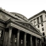 Black and white photo of two classical stone buildings with columns and ornate architectural details.