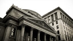 Black and white photo of two classical stone buildings with columns and ornate architectural details.