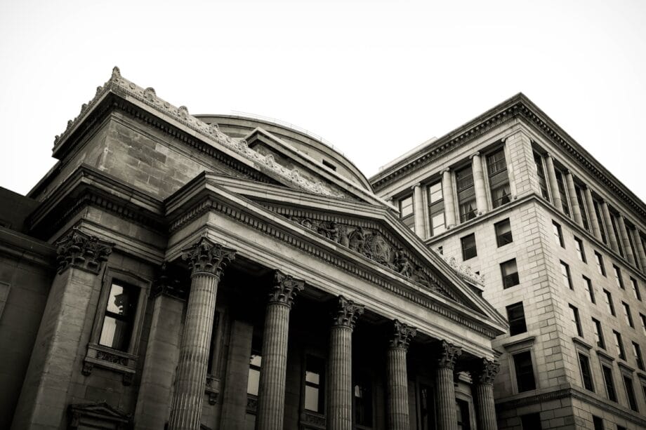 Black and white photo of two classical stone buildings with columns and ornate architectural details.