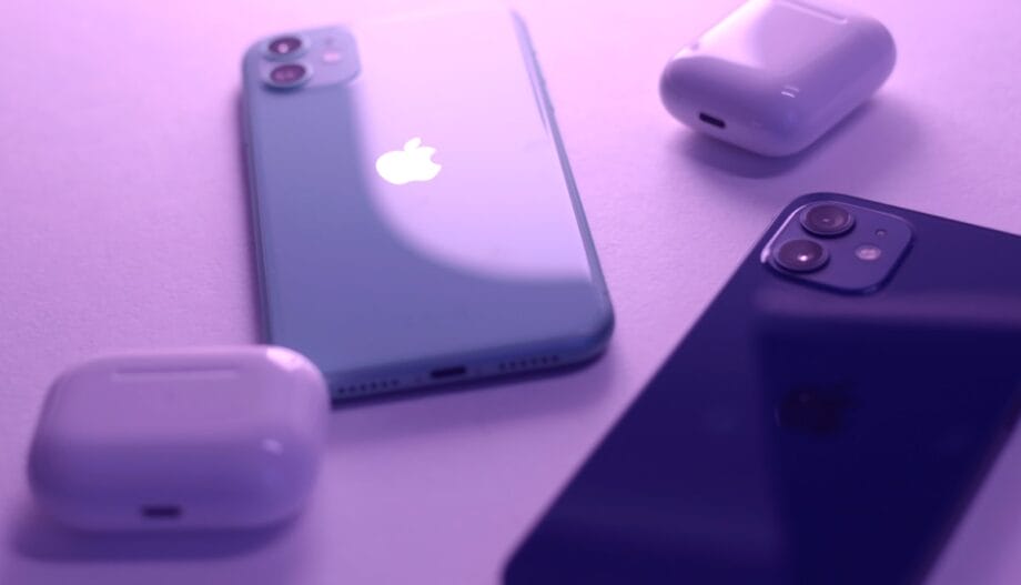 Two iPhones and two AirPods cases are placed on a flat surface under purple lighting.