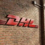 Red DHL logo mounted on a brick wall next to a large industrial-style window and a closed metal garage door.