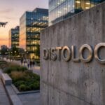 Modern office buildings at sunset, with people walking and a drone flying near a concrete wall labeled DISTOLOGY.