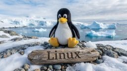 A penguin plush toy sits on rocks near a wooden sign reading Linux, with icebergs and snowy landscape in the background.