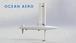 A white autonomous sail-powered marine drone with a vertical sail and rudder, labeled Ocean Aero on a plain background.