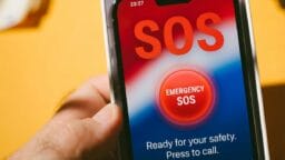 A hand holds a smartphone displaying an Emergency SOS screen with instructions to press to call for safety assistance.