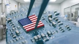 A chip with the American flag design is held by tweezers above a circuit board in a clean, modern lab setting.