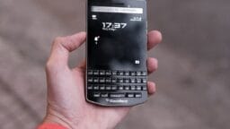 A person holds a BlackBerry Porsche Design smartphone with a physical keyboard and screen displaying the time.