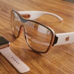 A smart watch and a pair of augmented reality glasses with white and gold accents are placed on a wooden surface.