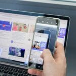 Person holding a smartphone to scan a QR code displayed on a laptop screen showing a website with social media content.