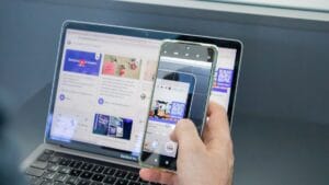 Person holding a smartphone to scan a QR code displayed on a laptop screen showing a website with social media content.