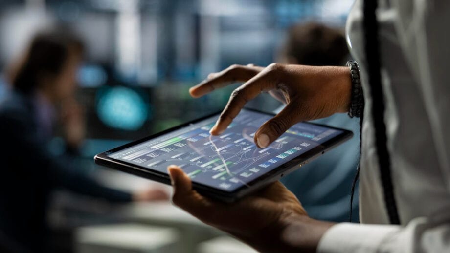 A person uses a tablet displaying data charts and graphs in a modern office setting.