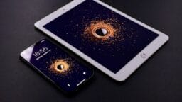 A smartphone and a tablet on a black surface, both displaying the same graphic of an orange swirl around a play button icon.