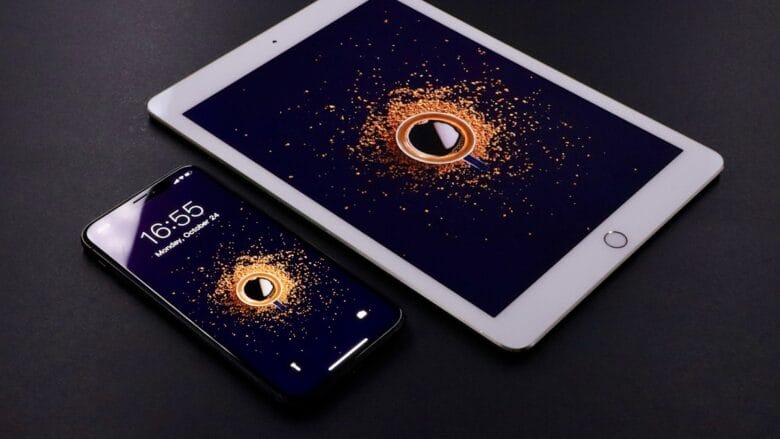 A smartphone and a tablet on a black surface, both displaying the same graphic of an orange swirl around a play button icon.