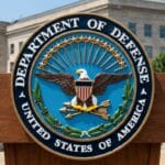 Podium with the seal of the U.S. Department of Defense in front of a government building and greenery.