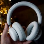 A hand holding a pair of white over-ear headphones with blurred lights in the background.