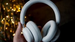 A hand holding a pair of white over-ear headphones with blurred lights in the background.