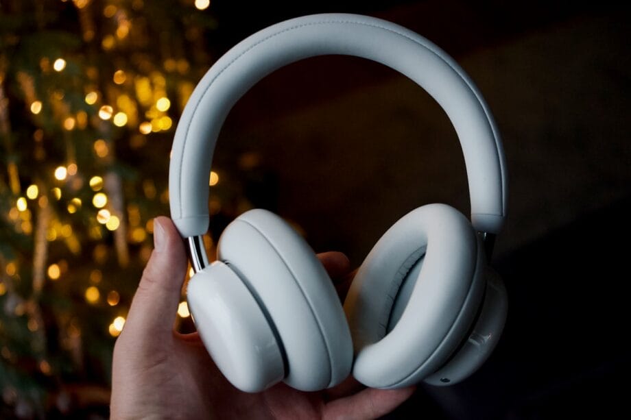 A hand holding a pair of white over-ear headphones with blurred lights in the background.