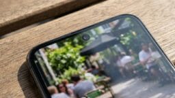 Close-up of a smartphone’s front camera with a blurred outdoor café scene displayed on the screen.