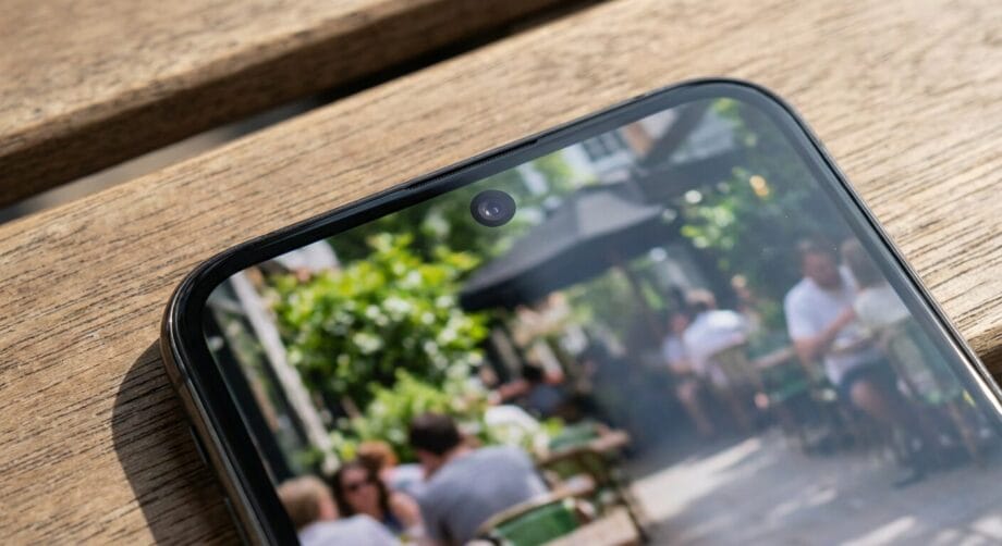 Close-up of a smartphone&rsquo;s front camera with a blurred outdoor caf&eacute; scene displayed on the screen.