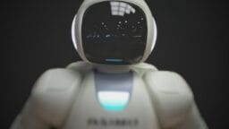 A white humanoid robot with a glossy black faceplate and glowing blue chest light, standing against a dark background.