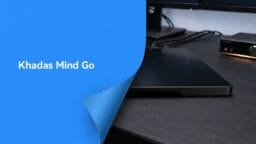 A Khadas Mind Go computer on a desk next to monitors and other electronic devices, with Khadas Mind Go text on a blue overlay.