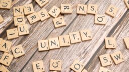 Scrabble tiles arranged to spell UNITY on a wooden surface, with other random letter tiles scattered around.