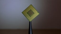 A computer processor chip held upright by black tweezers against a blurred background.