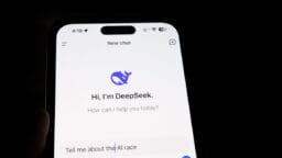 A smartphone screen displays an AI chatbot app called DeepSeek, with the prompt “Tell me about the AI race” entered.