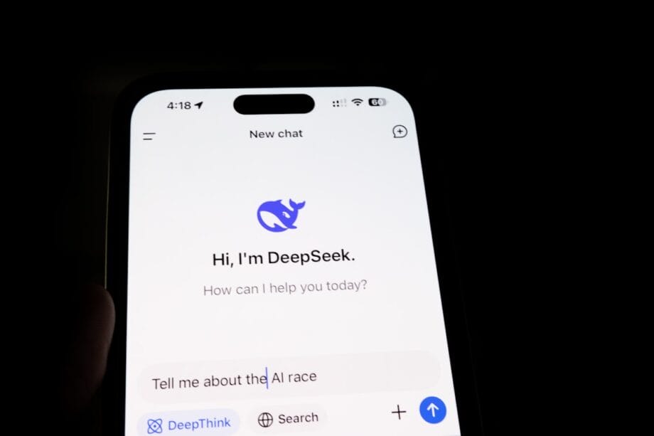 A smartphone screen displays an AI chatbot app called DeepSeek, with the prompt “Tell me about the AI race” entered.