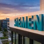 Siemens company building with large logo on facade, modern architecture, and sunset sky in the background.