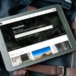 A tablet displaying the Unsplash website rests on top of a black and brown travel bag.