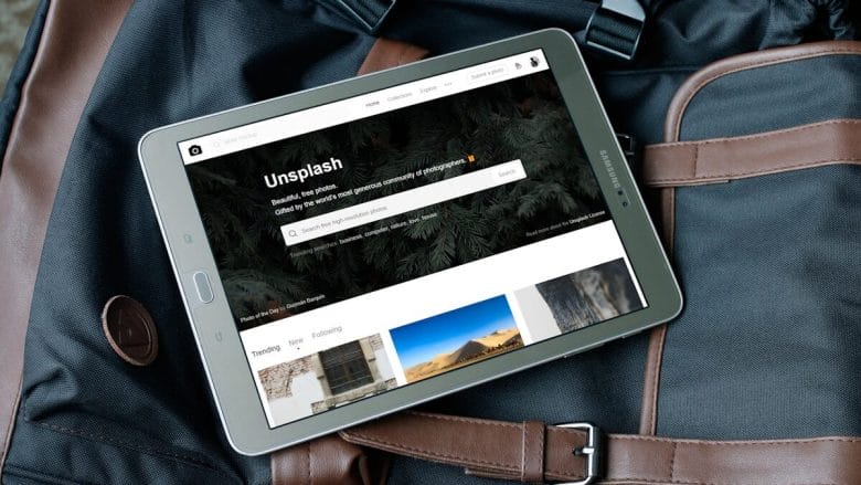 A tablet displaying the Unsplash website rests on top of a black and brown travel bag.