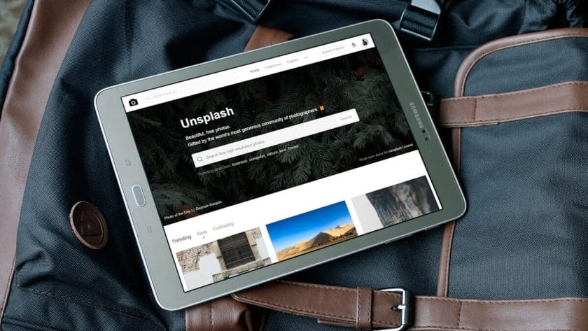 A tablet displaying the Unsplash website rests on top of a black and brown travel bag.