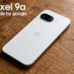 A white Google Pixel 9a smartphone lies face down on a wooden surface with text Pixel 9a made by google in the top left corner.