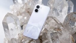 A white Oppo smartphone with dual cameras is placed upright among large clear quartz crystals.