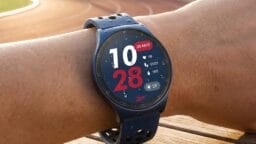 A person wearing a blue smartwatch showing the time, date, weather, heart rate, steps, and calories burned at an outdoor track.