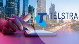 A hand touches a tablet with a cityscape background, overlaid with the Telstra logo and text.