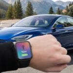 A person holds up a smartwatch displaying Tesla Active near a blue Tesla car parked on a mountain road.