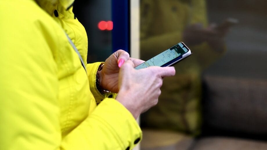 Person in a yellow jacket using a smartphone while standing next to a glass window.