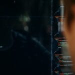 A person looks at a computer screen displaying lines of code in a dark-themed text editor.