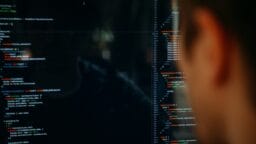 A person looks at a computer screen displaying lines of code in a dark-themed text editor.