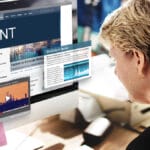 A person sits at a computer displaying news articles, stock market data, and a video about content on the screen.