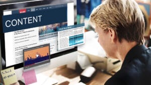 A person sits at a computer displaying news articles, stock market data, and a video about content on the screen.
