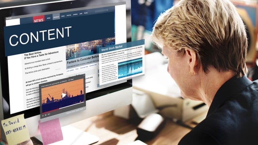A person sits at a computer displaying news articles, stock market data, and a video about content on the screen.